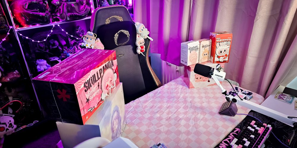 A picture of my stream room with a popup desk covered in a pink checkered bedsheet for vibes. On top is some POP MART merch ready to unbox! 
