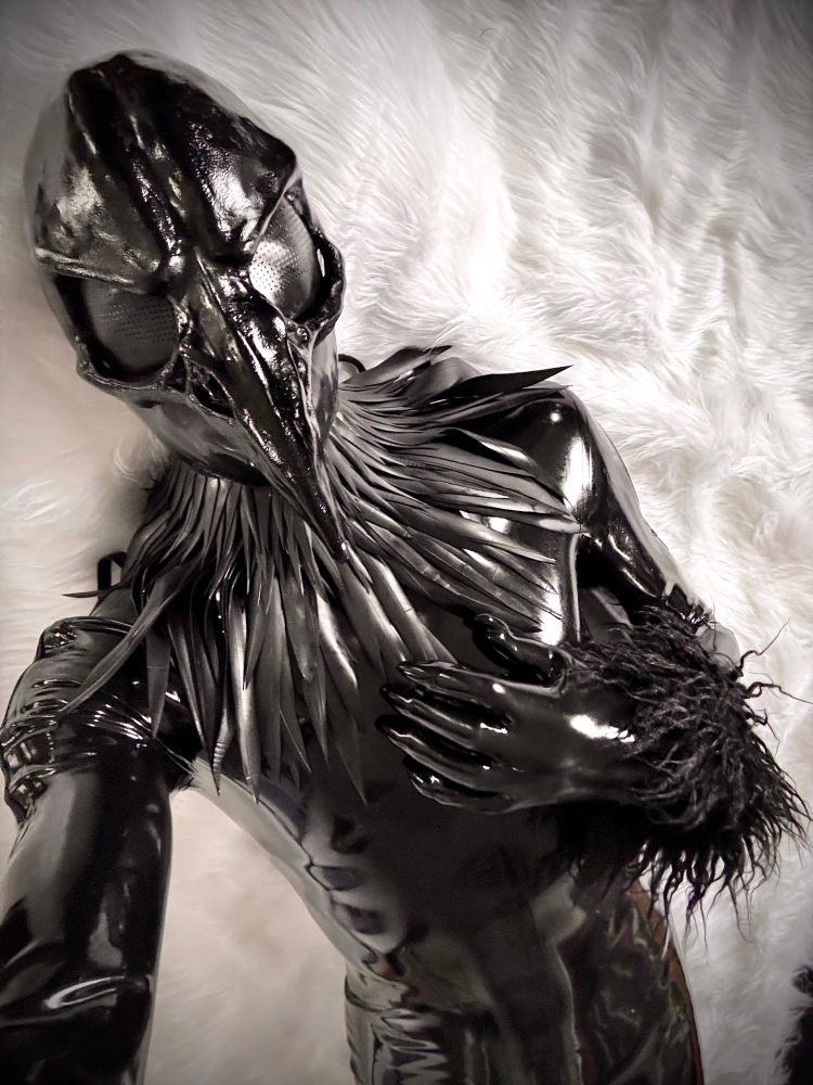 A shiny black rubber bird lounges on a white fur blanket.