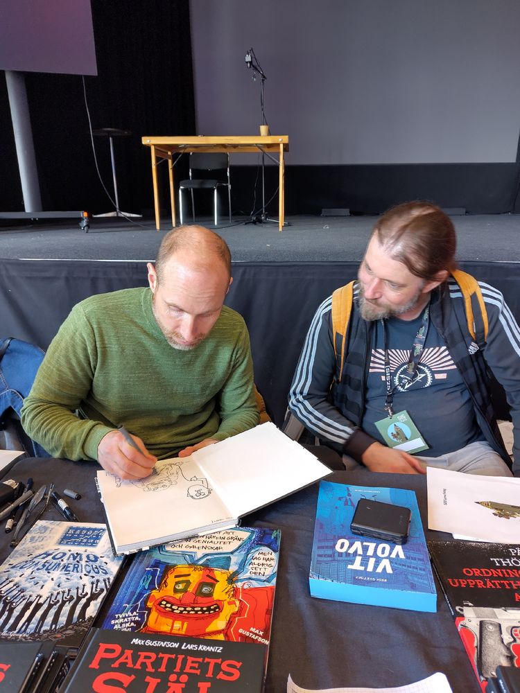 Max Gustafson signerar serieboken Partiets själ medan Lars Krantz tittar på