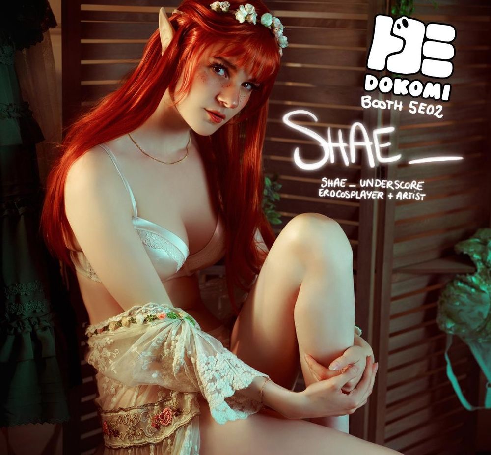 Shae as a redhead elf sitting. 
Text on the photo says:
Dokomi Booth 5E02
Shae_
Shae_Underscore 
Erocosplayer + Artist