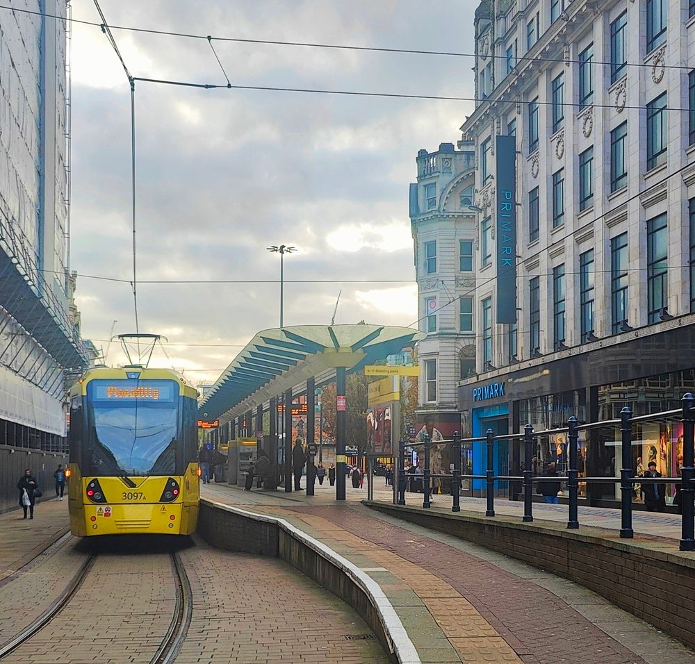 A yellow tram stopped on a broad street beside a Primark store and Victorian buildings