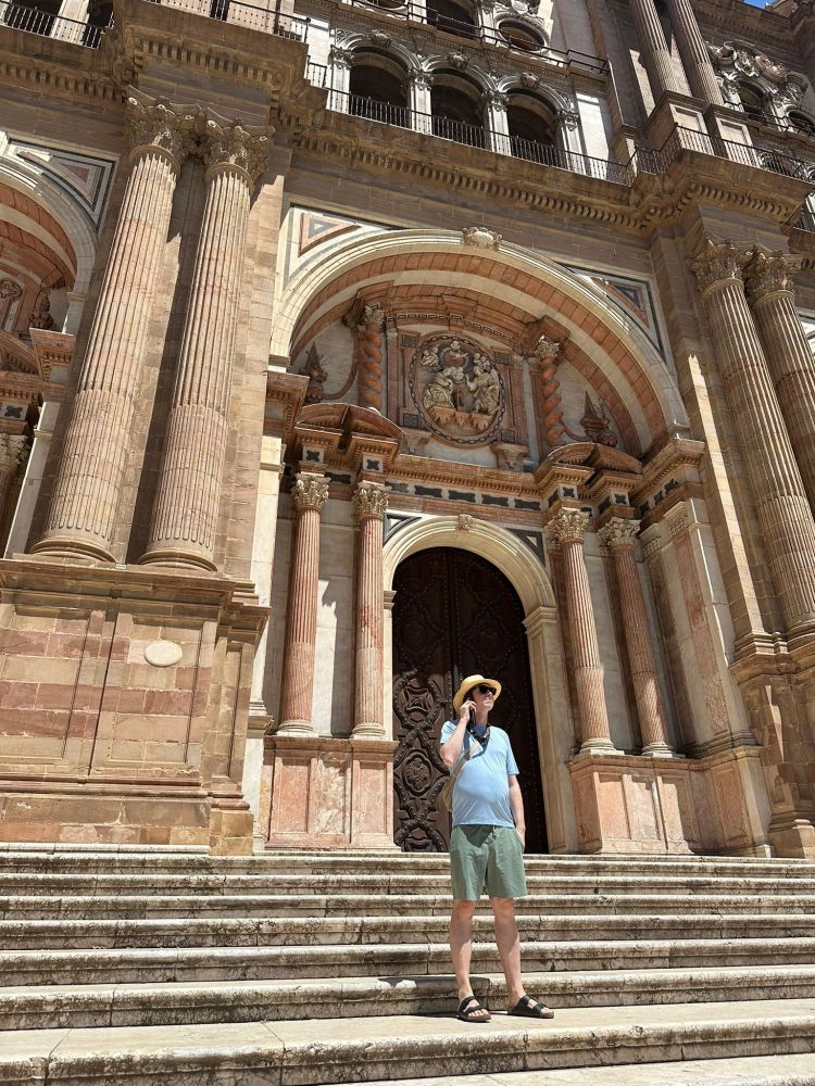 Calum outside a Cathedral entrance in bright daylight holding an audio guide 