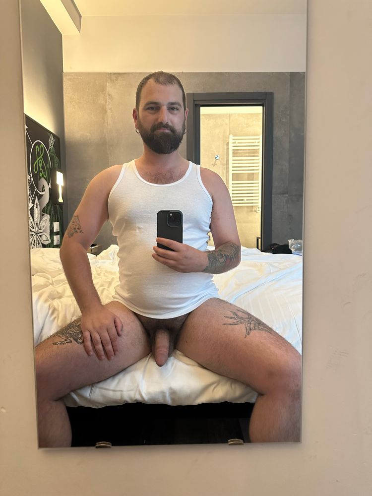 Mirror selfie in a hotel in Milan. I’m sitting on the edge of the bed, wearing a white tank top and nothing else. My dick is hanging out and semi hard.