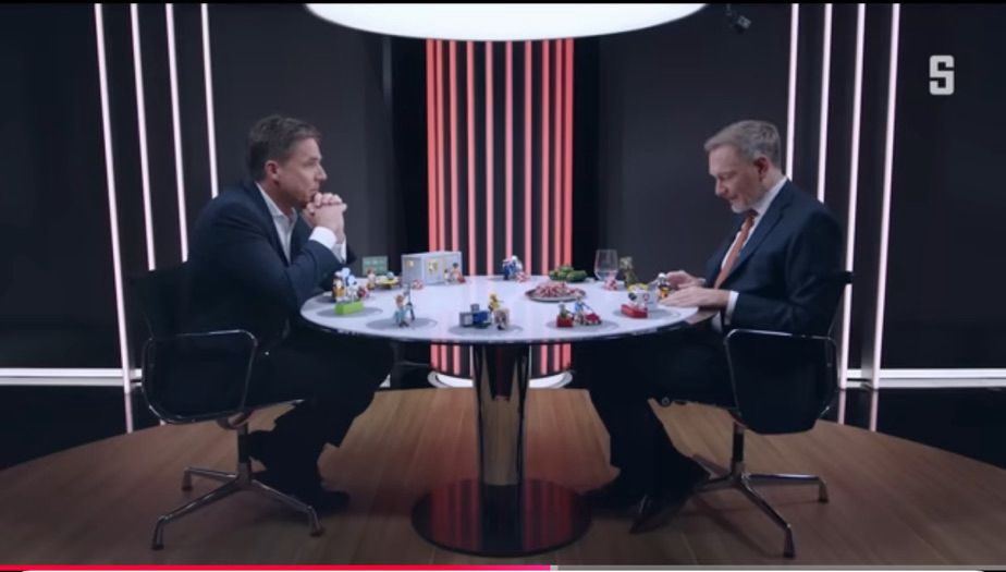 Markus Feldenkirchen (Spiegel) und Christian Lindner sitzen an einem Tisch mit Playmobil-Figuren