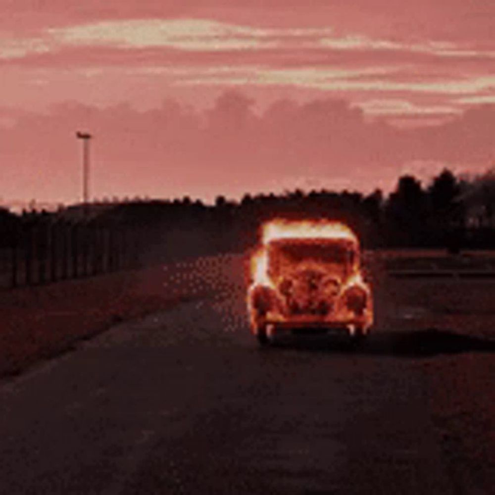 a burning car is driving down a road with a sunset in the background .