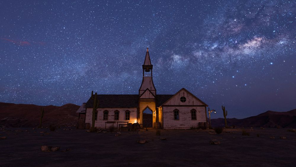 An old church dimly illuminated by a front light under a bright star-filled sky.