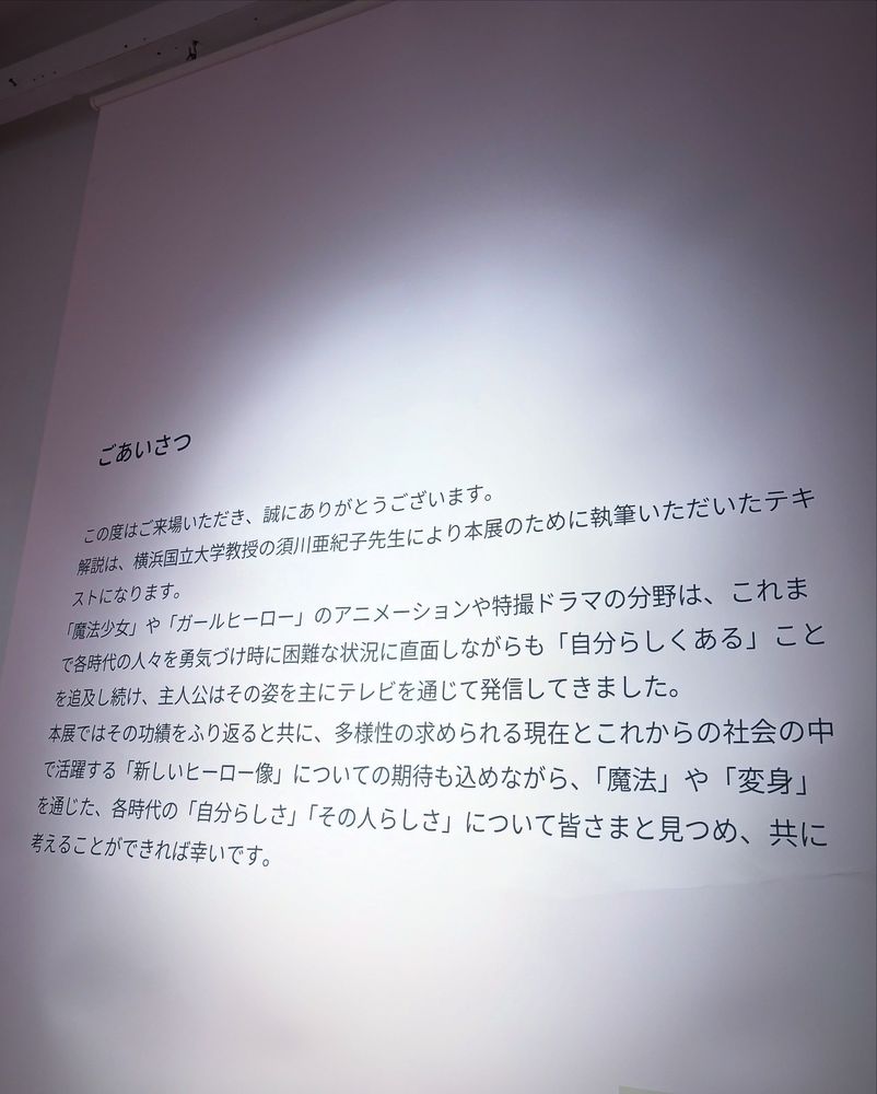 企画展のあいさつ文章。
「ごあいさつ
この度はご来場いただき、誠にありがとうございます。
解説は、横浜国立大学教授の川亜紀子先生により本展のために執筆いただいたテキストになります。
「魔法少女」や「ガールヒーロー」のアニメーションや特撮ドラマの分野は、これまで各時代の人々を勇気づけ時に困難な状況に直面しながらも「自分らしくある」ことを追及し続け、主人公はその姿を主にテレビを通じて発信してきました。
本展ではその功績をふり返ると共に、多様性の求められる現在とこれからの社会の中で活躍する「新しいヒーロー像」についての期待も込めながら、「魔法」や「変身」を通じた、各時代の「自分らしさ」「その人らしさ」について皆さまと見つめ、共に考えることができれば幸いです。」と書かれている。