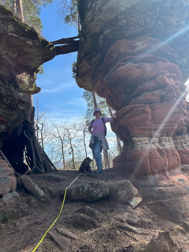 Felsformation aus zwei Türmen, dazwischen eine Lücke wie ein Tor. Dort steht eine Frau und ein Hund liegt auf dem Boden.