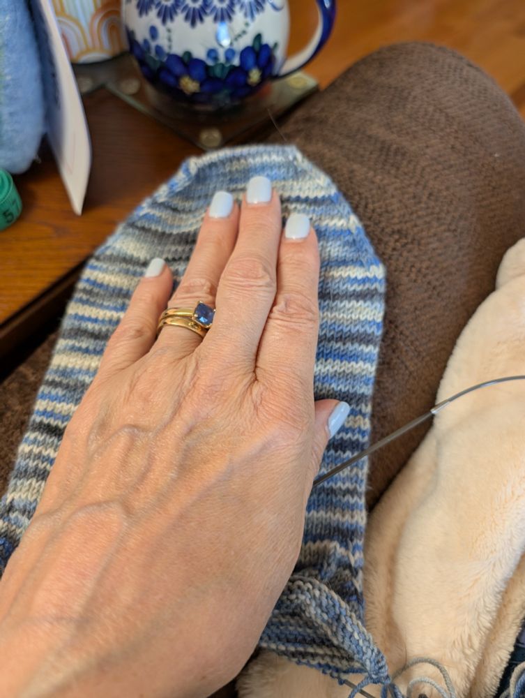 A hand on top of a much TOO large blue and grey sock.