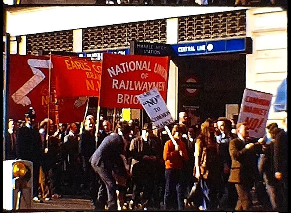 Men and women marching along the street, holding up placards reading 'Common Market No!' and 'Say "No" to Common Market' and also holding up union banners such as the National Union of Railwaymen Brighton branch.