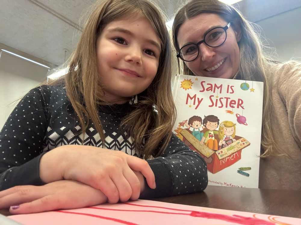 Mother and daughter smiling while holding a book titled "Sam is my Sister"