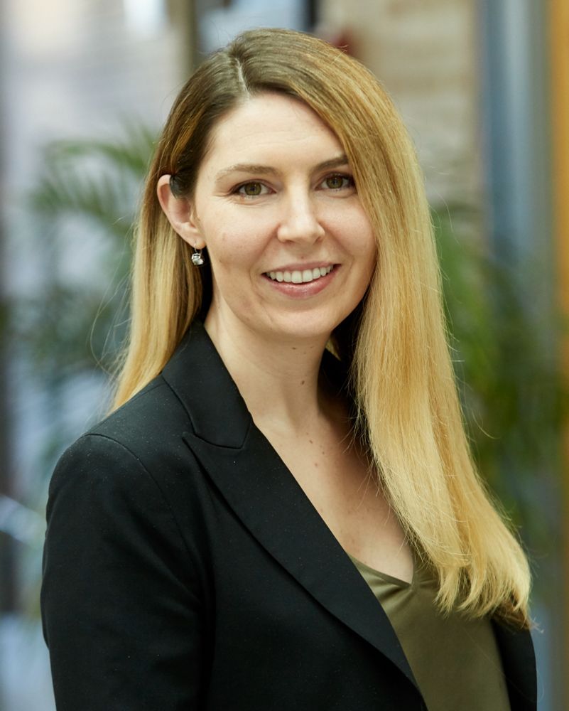 Brittany Charlton wearing a black suit and green shirt, blonde hair, smile