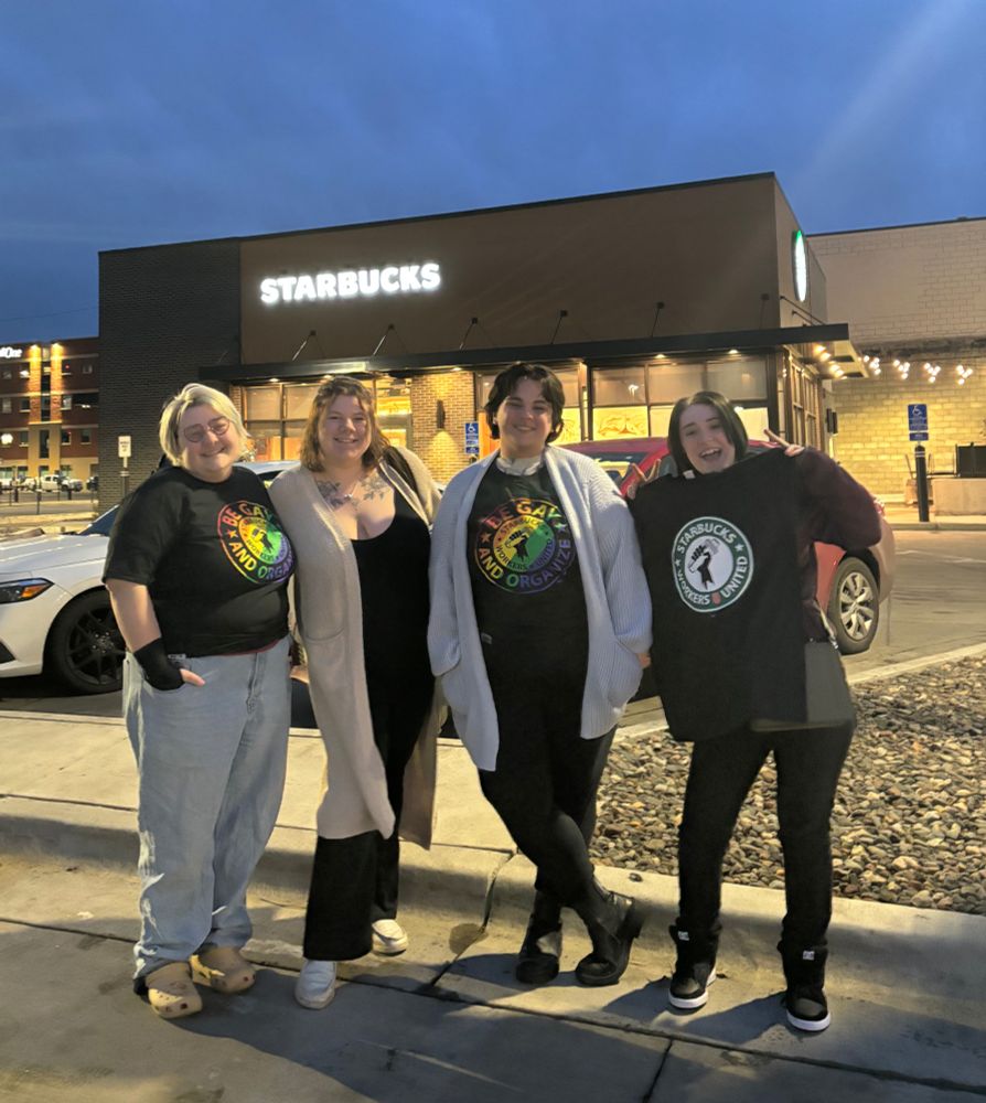 Four SBWU members pose, celebrate, and don union shirts in front of their Starbucks store