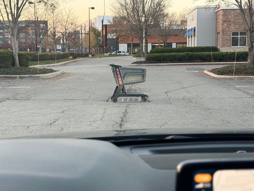 A shopping cart in the middle of a parking lot, where the cars drive 
