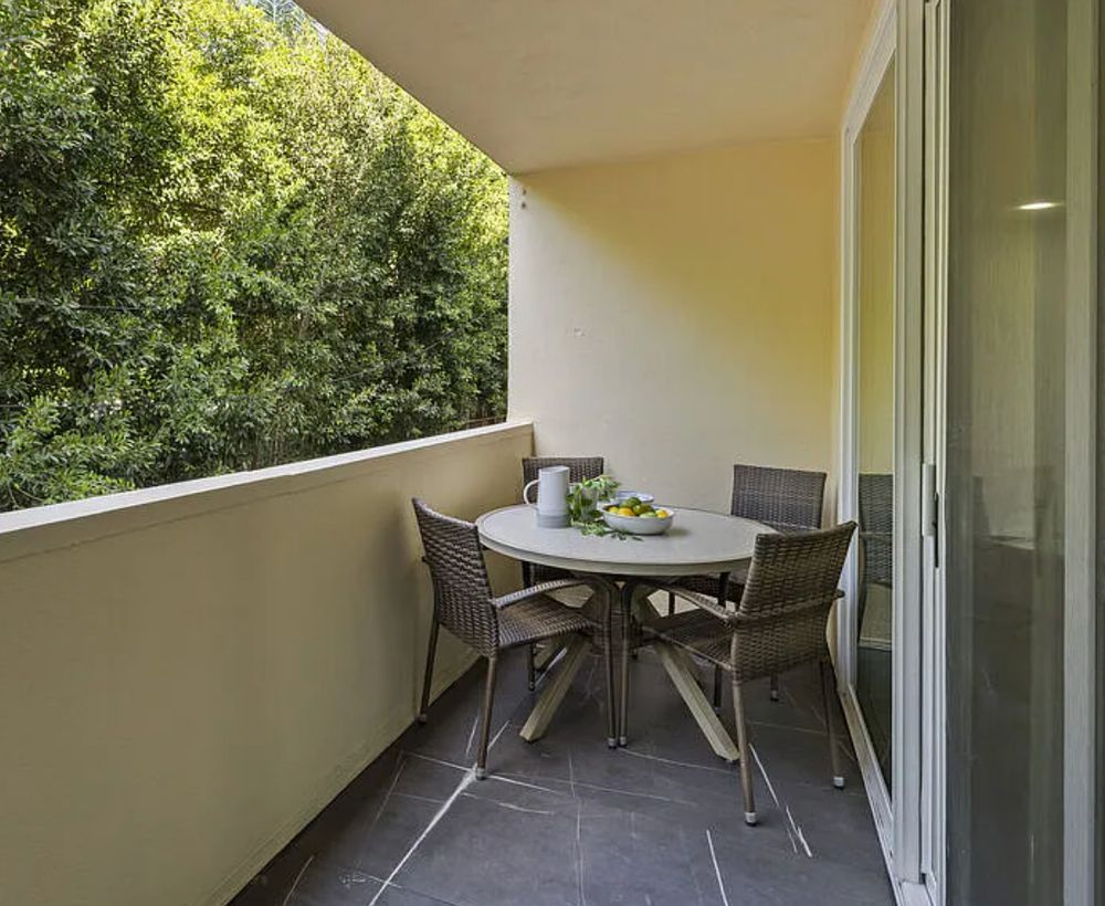 A table and chairs set up on a balcony of an apartment. Except the balcony is so narrow that there is literally no room for a person to get to the chairs on the other side of the table or to pull out the chairs on the near side of the table. 