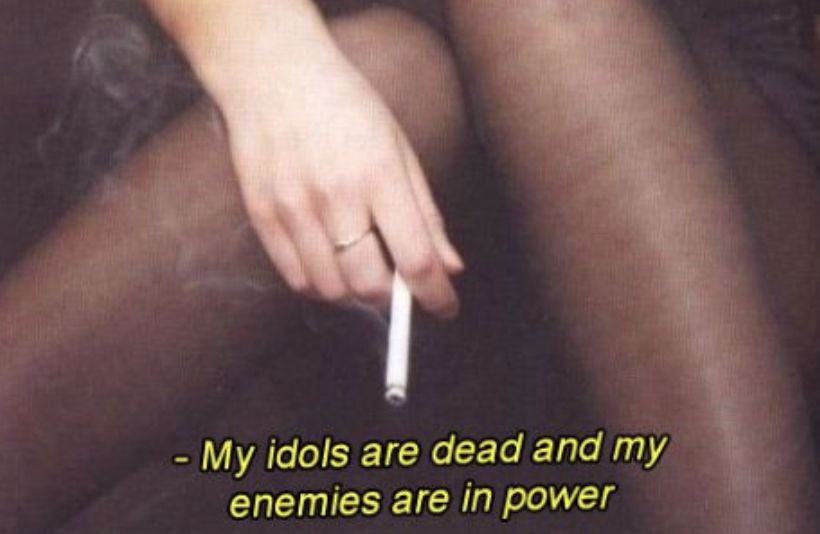 "My idols are dead and my enemies are in power" written over a photo of a woman's hand holding a cigarette by her legs. 