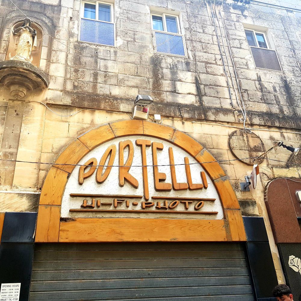 Orange & white 'Portelli Hi-Fi-Photo' shop sign in 60's retro typeface on a Maltese street.