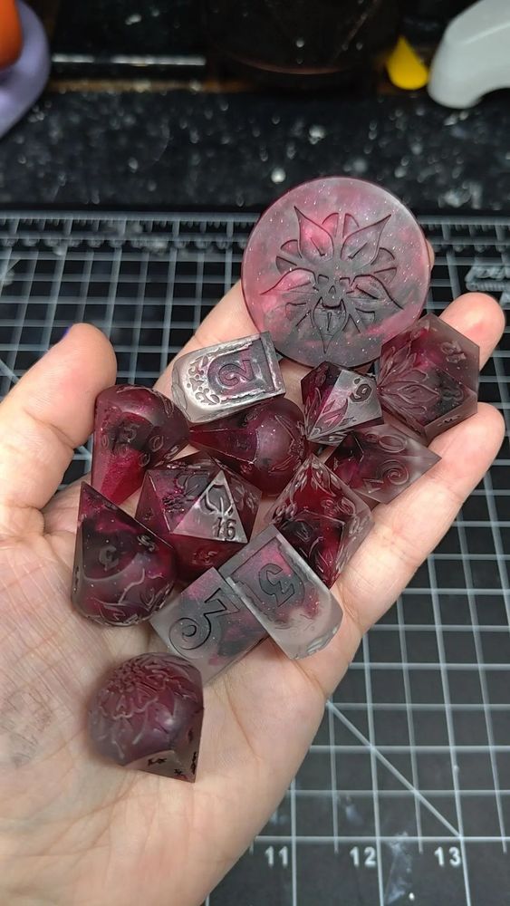 13 different shaped dice with flowers and leaves etched into the dice faces. they are made with a mix of clear, crimson, and black resin.