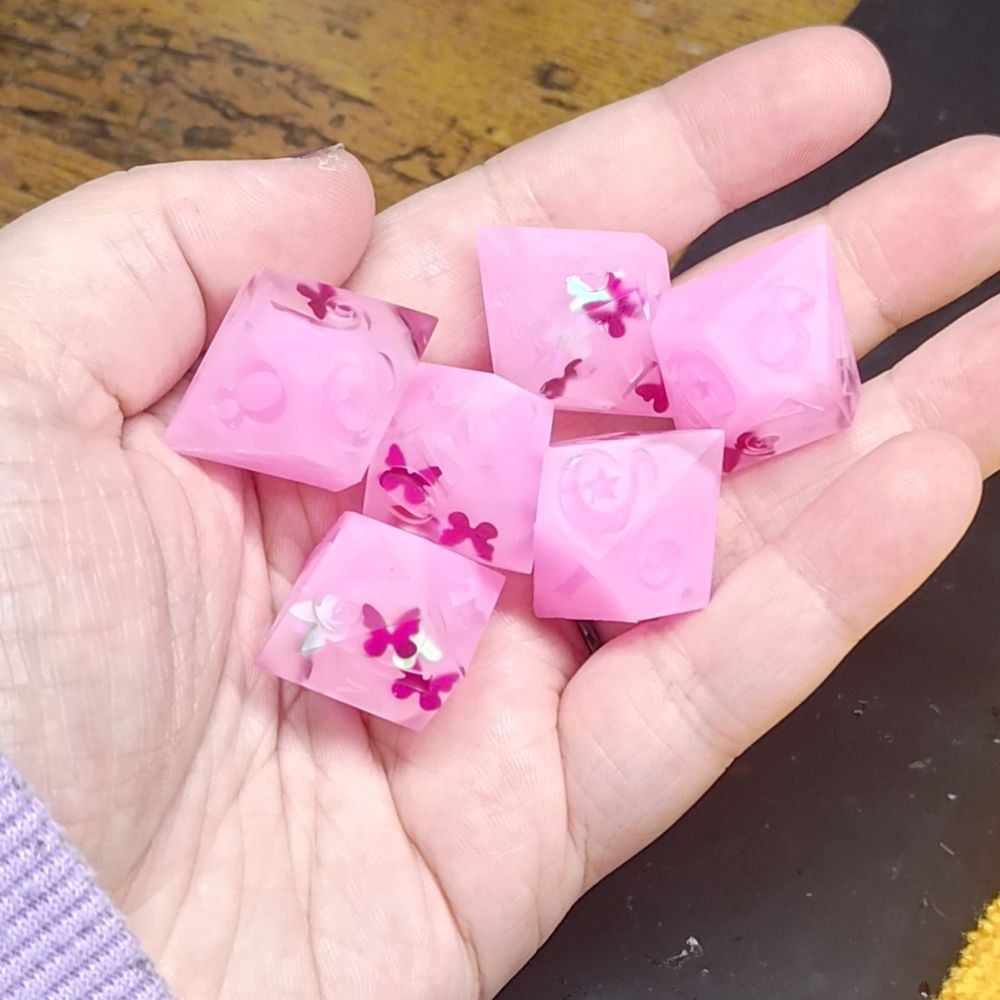 6-d10 dice that are matte and in an unfinished state. the dice are pink overall, with darker pink butterflies showing through.