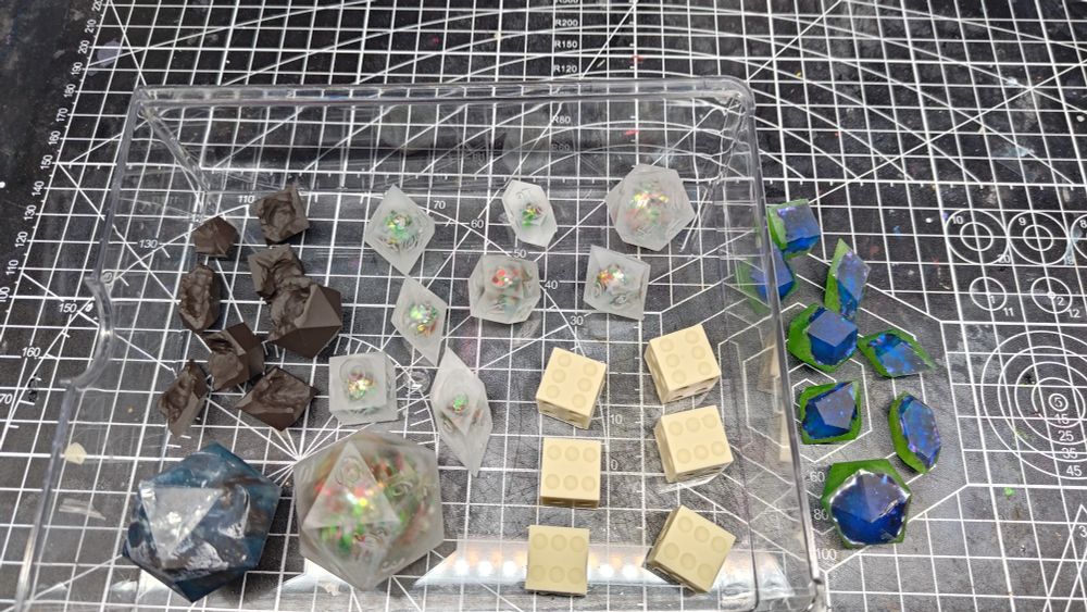 Matte, unfinished dice. There is an assortment of different shapes, colors, and sizes of dice, sitting in a clear tray.
