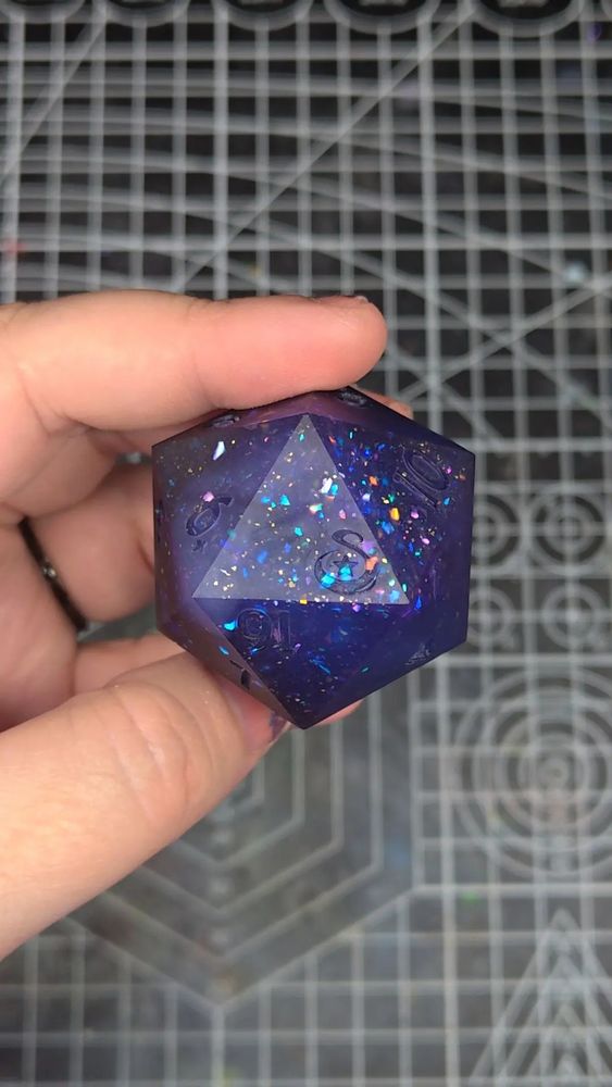 A large 45mm D20 that looks like the night sky with intense sparkles and a dark blue/purple resin base. This d20 is matte and unfinished.