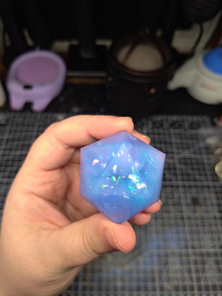 a chonky d20, 45mm in size. there are flecks of reflective material inside of the d20. the overall look gives off cute, sweet, cotton candy vibes.