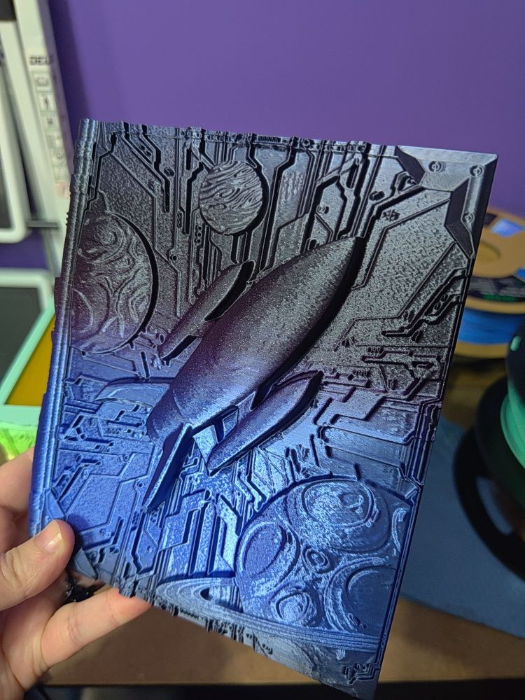 A 3D printed storage tome for not only TTRPG players, but you can use them for anything! The outside tome has a unique design, while the faux pages hide the secret storage compartments. This tome has a 3D image of a rocket ship, with planets and futuristic textures on the cover. The filament used is a gradient filament that goes from black to blue to purple, and has sparkly glitter mixed into the filament.