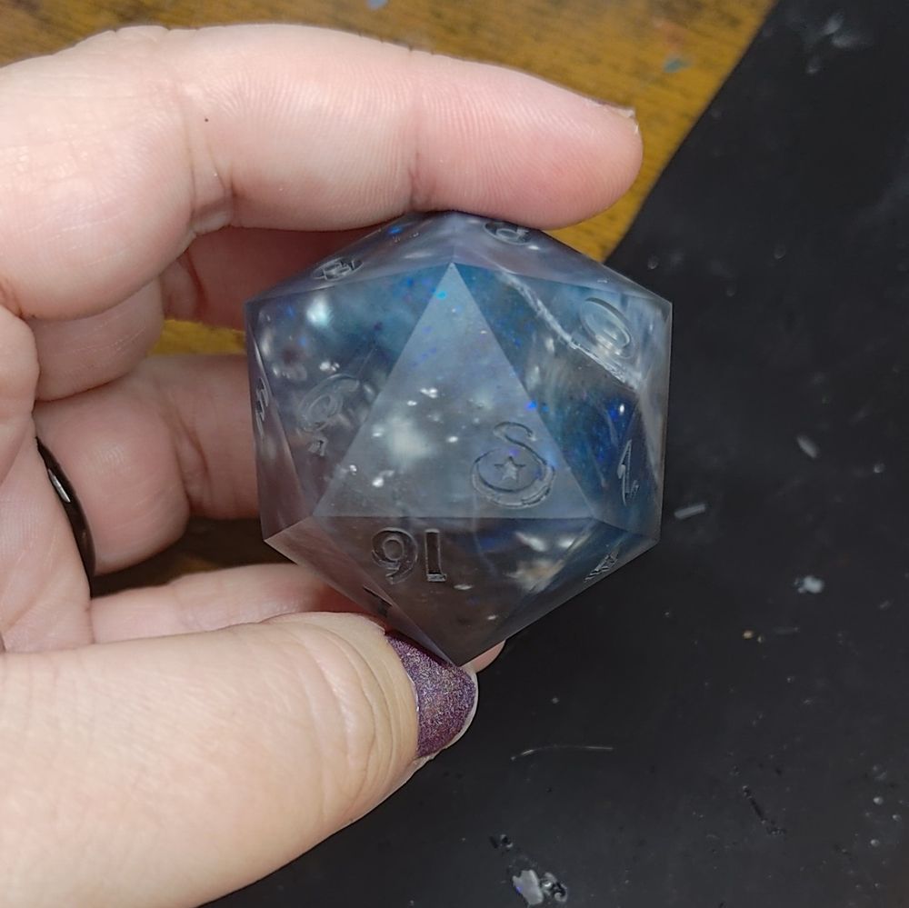 a large, 45mm D20, matte and unfinished. the high face is marked with a swirly S and a star.