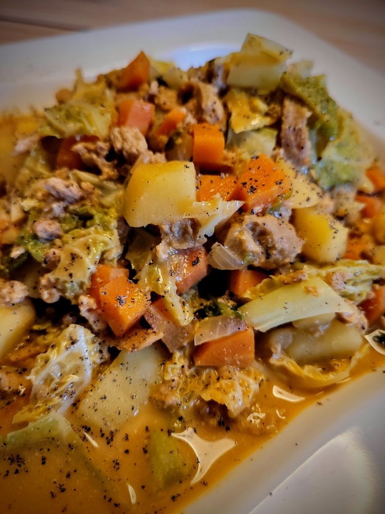 Auf einem Teller ist ein Wirsingeintopf mit Kartoffeln, Möhren, veganen Hack + Speck samt Curry-Sauce