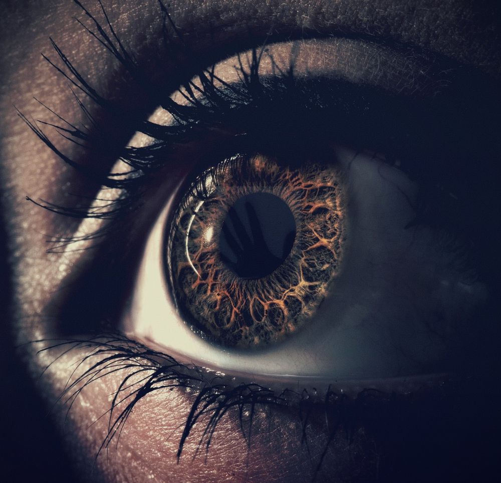 A close-up of a woman's eye, wide open as we see a ghostly hand reflected in her pupil.