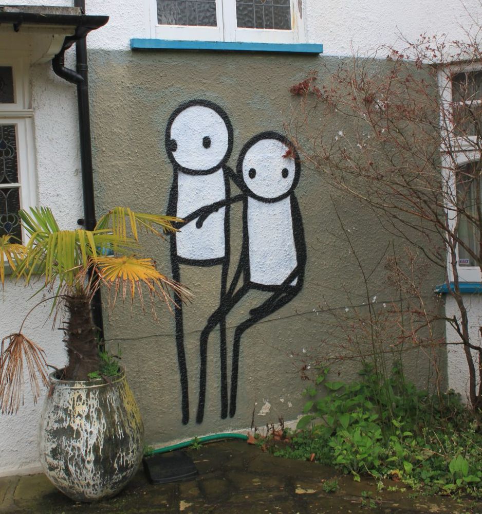 Two stick figures, one seated, on a house wall. A street art representation of The Linley Sisters by Stik