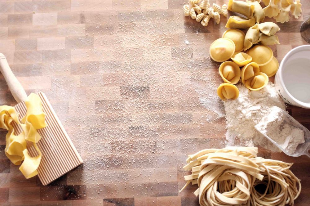 A floured tabled with a combination of handmade pasta shapes and tools