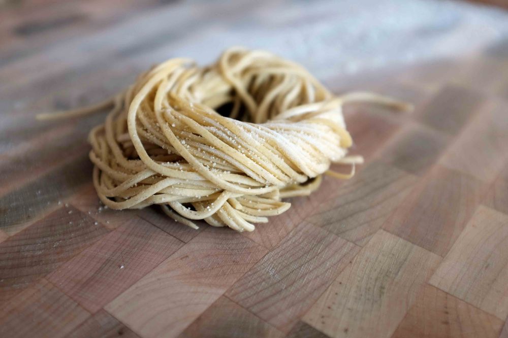 A roll of handmade spaghetti on a floured wooden table