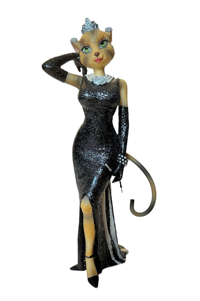 An image of an anthropomorphic cat figure. It’s dressed in a long black gown with a slit leg and wearing long evening gloves that extend up to the elbow. The cat has long eyelashes and is wearing lipstick. It is also wearing a silver crown, silver flower earrings on the back of its ears, and a matching pearl necklace and bracelet. It holds a long cigarette holder in its left hand