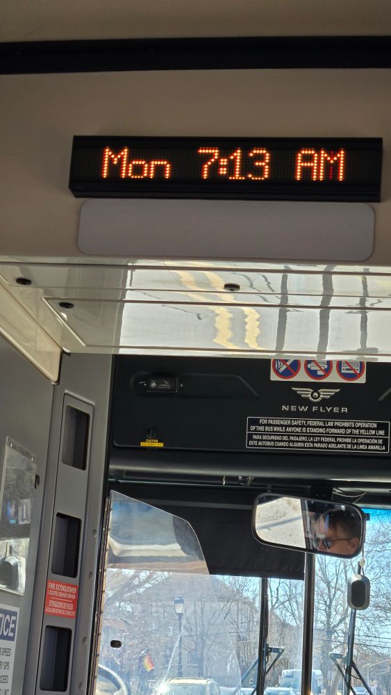 The inside of a local bus displaying Monday 7:13AM. 