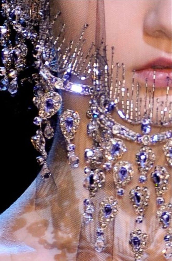 Foto de la mitad del rostro de una chica de piel blanca que está cubierto por un finisimo velo transparente cubierto de pedrería azul. 