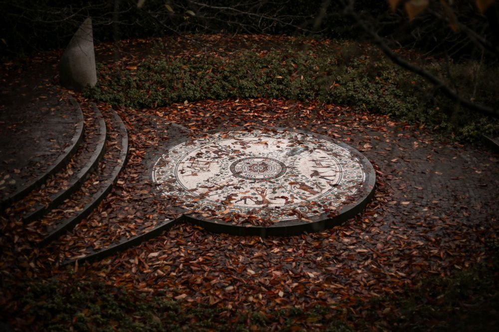 Circular mosaic on the Roman gardens in Chester. Details of the mosaic aren't quite visible, but the mosaic is surrounded by autumnal orange leaves.