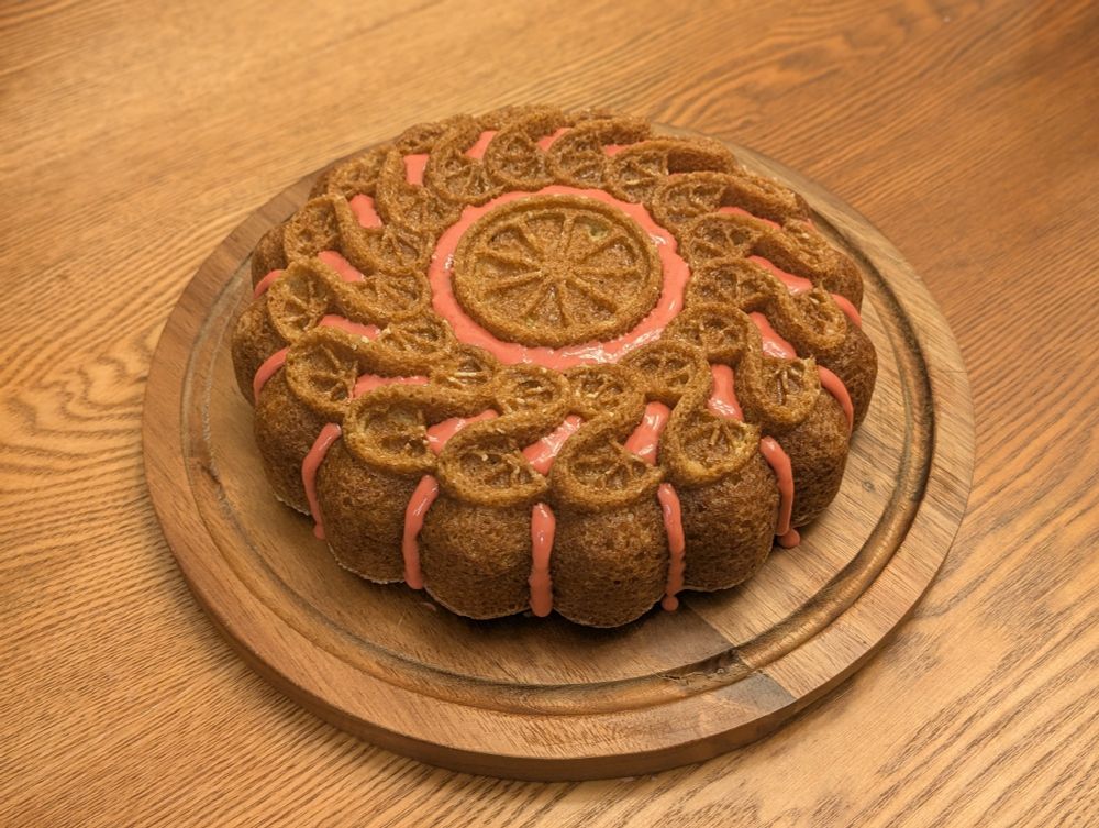 Olive oil cake baked with an intricate citrus pattern and pink glaze accents 
