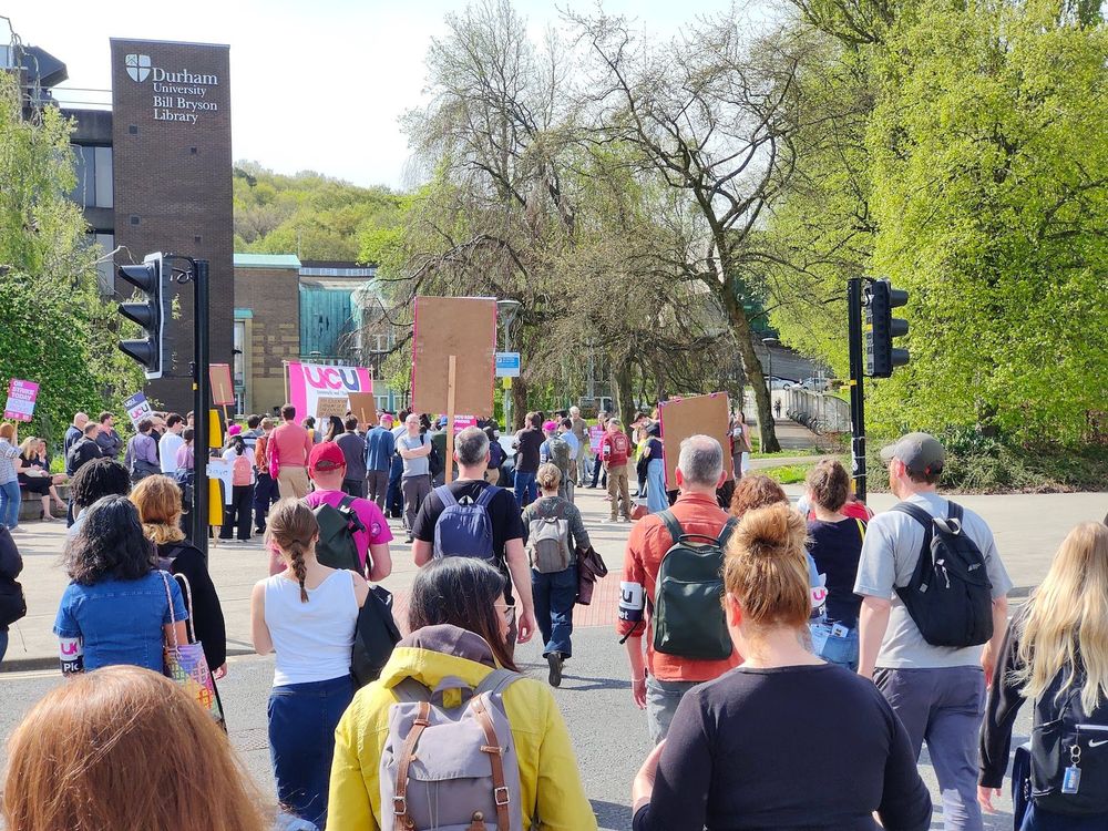 Durham UCU members with placards and armbands gather for a rally outside the Bill Bryson library. We are in a trade dispute over University management's plan to cut £20M in staff costs over the next two years. Staff cuts are unnecessary and threaten our capacity to deliver world-class teaching and research. Sign the petition to let Durham University management know you oppose staff cuts. 