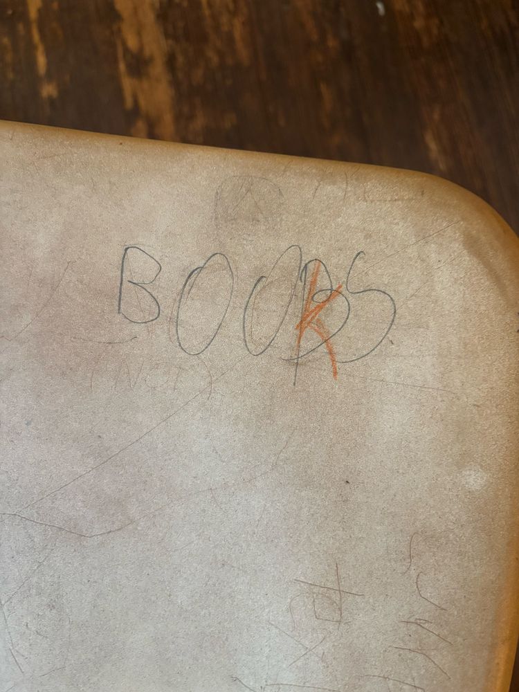 "Boobs" scratched into a classroom chair but someone tried to write a "K" over the second  "B" so it says "Books"