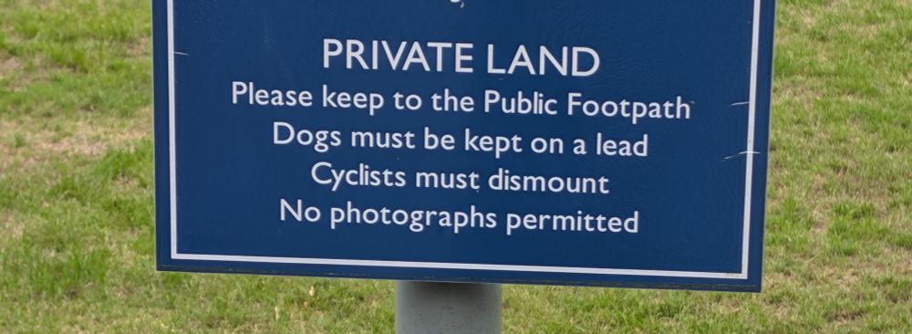 A sign reading in part:
Private Land
Please keep to the public footpath
No photographs permitted