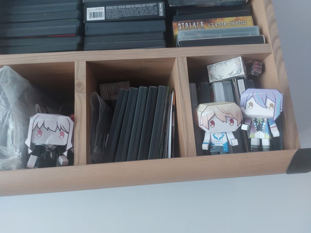 Photo of a shelf with project sekai papercraft dolls sitting on it. Rui and Tsukasa are standing together while Mizukie stands off to the side.