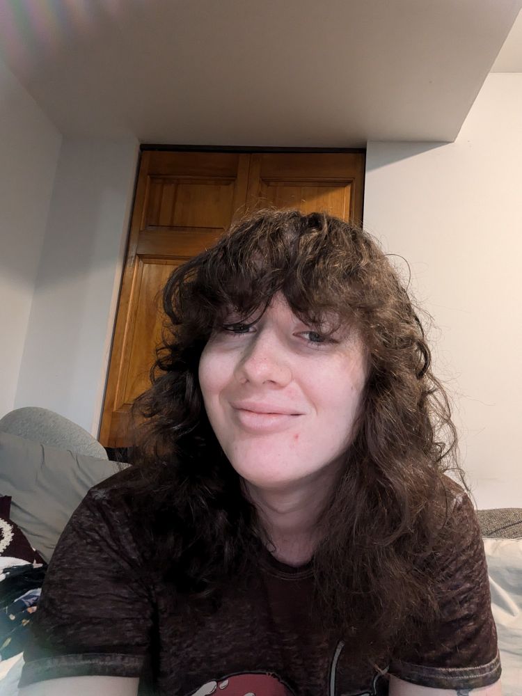 Autumn is showing off her new haircut which is a wolf cut with bangs. The color of the hair is a dark brown. She is smiling 