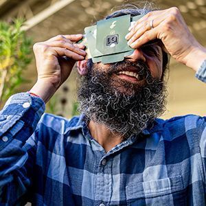 Manu Prakash, a bearded man, holds a paper-made microscope