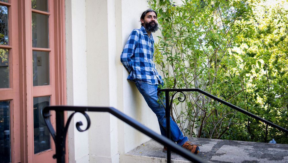 Manu Prakash, a bearded man in plaid and a bioengineer, leans against a wall outside 