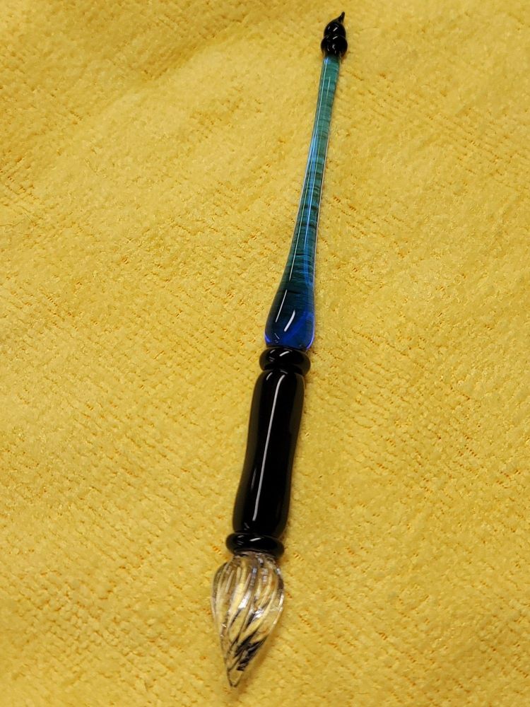 A glass dip pen. The clear glass nib resembles bristles on a brush. The body of blue glass is in the shape of a droplet.