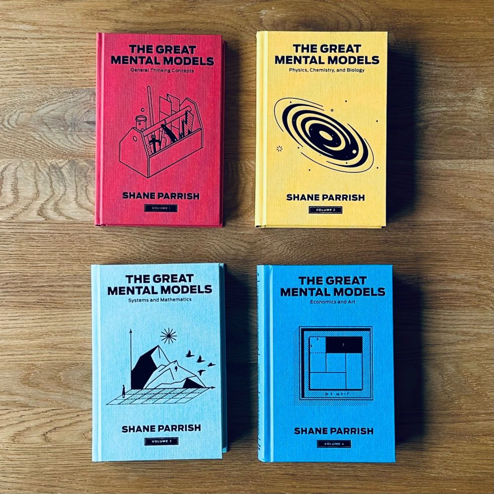 The image shows the four books in the "Great Mental Models" series by Shane Parrish on a table. Book 1 is about general thinking concepts; book 2 is about physics, chemistry and biology; book 3 is about systems and mathematics; and book 4 is about economics and human behaviour.