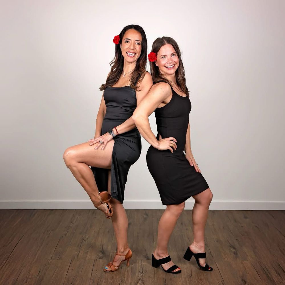 Vivian and Tracy pose in black dresses and smiling faces. They have red flowers in their hair.