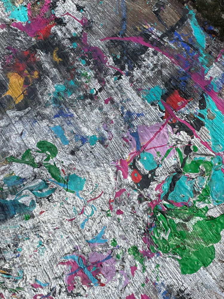 Paint spatters in green, blue, pink and yellow on the pavement 