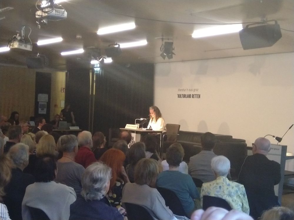 Foto von Natascha gangl die auf der Bühne des Literaturhaus Graz liest vor vollem Saal 